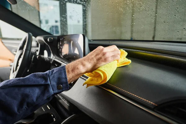Cropped view of dedicated specialist in blue uniform cleaning glove compartment in car with rag — Stock Photo