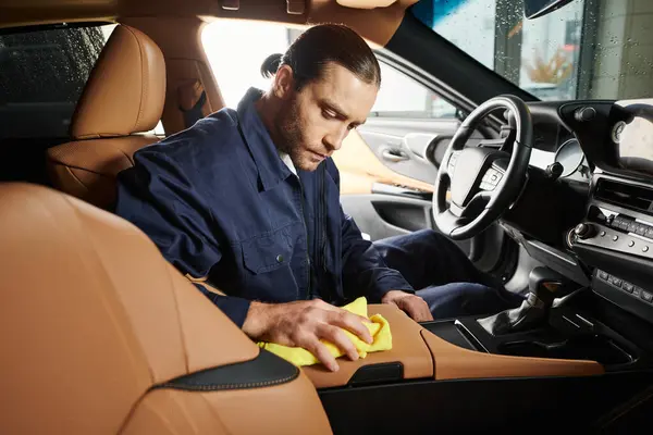 Appealing devoted serviceman in blue uniform with collected hair cleaning car with yellow rag — Stock Photo