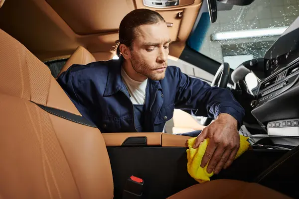 Trabajar duro especialista de buen aspecto con el pelo recogido en la limpieza uniforme coche moderno con trapo - foto de stock