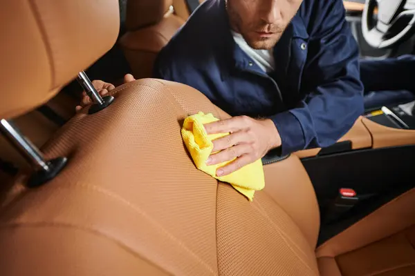 Vue recadrée de travailleur dévoué en bleu confortable uniforme nettoyage attentif voiture avec chiffon jaune — Photo de stock