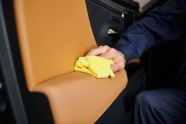 Cropped view of hard working dedicated specialist in blue uniform cleaning car with yellow rag — Stock Photo