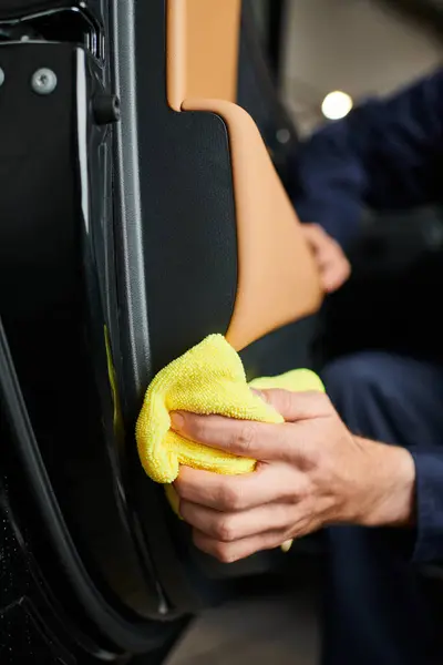 Cropped view of dedicated professional serviceman in blue uniform cleaning car with yellow rag — Stock Photo