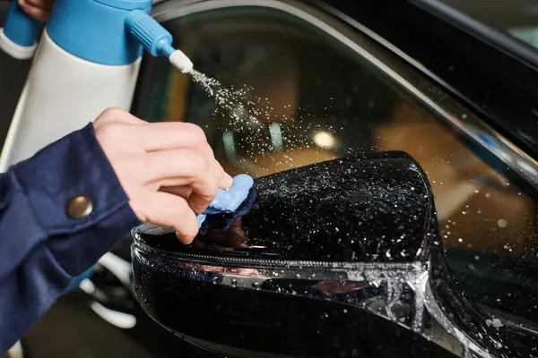 Cropped view of dedicated serviceman using pulverizer and rag to clean side view mirror of car — Stock Photo