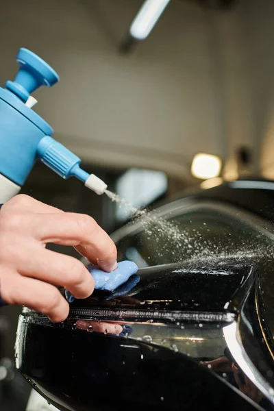 Cropped view of hard working man in uniform cleaning side view mirror using pulverizer and rag — Stock Photo