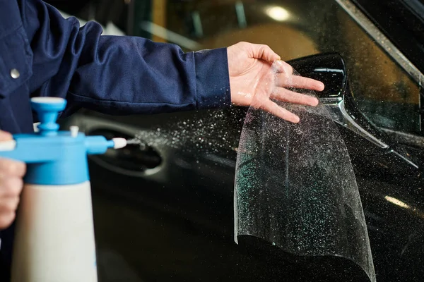 Visão recortada de profissional dedicado em azul uniforme confortável aplicando folha protetora no espelho do carro — Fotografia de Stock