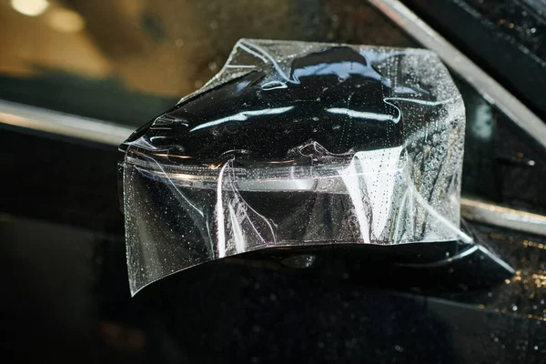 Объектная фотография бокового зеркала черного нового авто с частично нанесенной защитной фольгой — стоковое фото