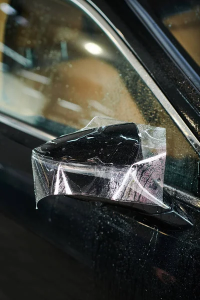 Объектное фото бокового зеркала черного современного автомобиля с частично нанесенной защитной фольгой — стоковое фото