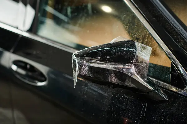 Об'єктна фотографія захисної плівки, нанесеної ретельно на дзеркало чорного сучасного автомобіля — стокове фото