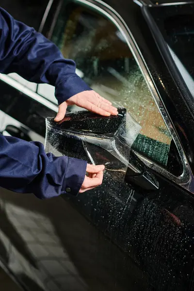 Cropped view of hard working professional serviceman in blue uniform applying protective foil on car — Stock Photo
