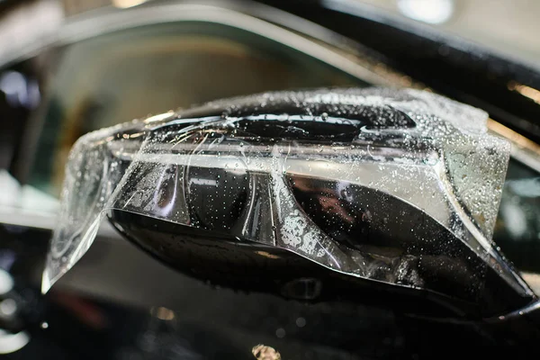 Об'єктна фотографія прозорої захисної фольги, нанесеної на бічне дзеркало чорного сучасного автомобіля — стокове фото