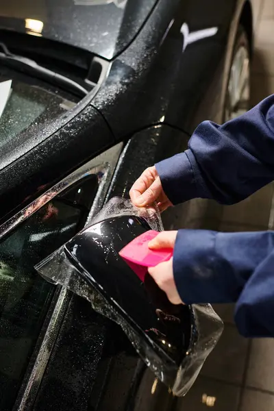 Cropped view of hard working professional worker applying transparent protective foil on black car — Stock Photo