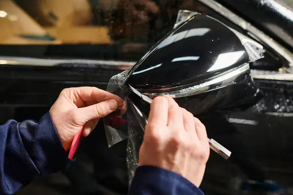 Cropped view of dedicated professional male worker applying protective foil on black car mirror — Stock Photo