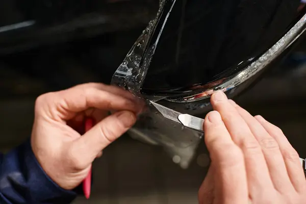 Visão recortada do trabalhador profissional que trabalha duro que aplica a folha protetora no carro preto na garagem — Fotografia de Stock