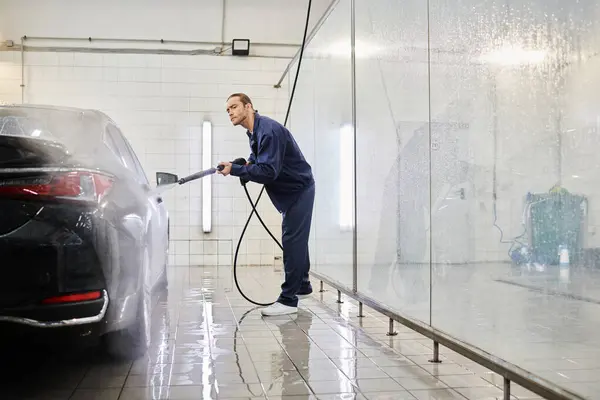 Handsome professional man in uniform with collected hair using hose to clean car in garage — Stock Photo