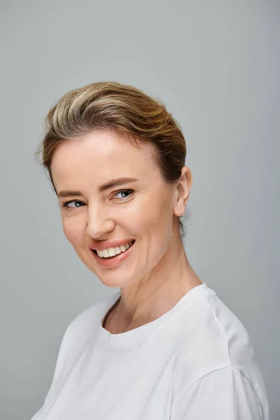 Jolly attractive woman with blonde hair and contact lenses posing on gray backdrop and looking away — Stock Photo