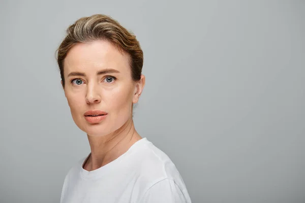 Attractive blonde woman with contact lenses and collected hair looking at camera on gray backdrop — Stock Photo