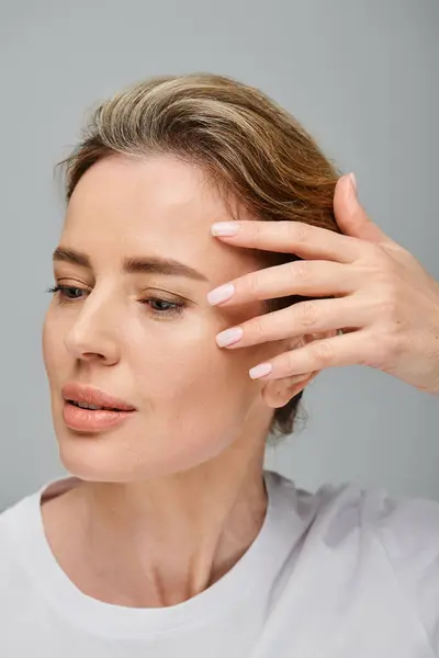 Mujer guapa con lentes de contacto y pelo rubio recogido mirando hacia otro lado sobre fondo gris - foto de stock