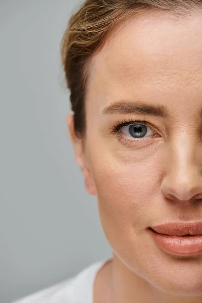 Fröhliche, gut aussehende Frau mit Kontaktlinsen und blonden Haaren, die vor grauem Hintergrund in die Kamera blickt — Stockfoto