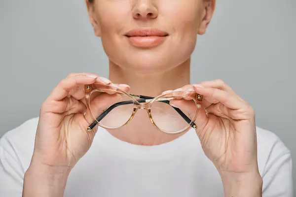Cropped view of jolly woman in casual attire holding glasses in front of her on gray backdrop — Stock Photo