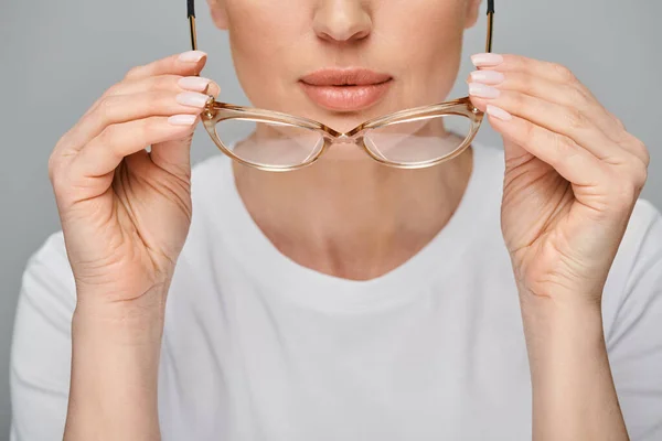 Cropped view of woman in casual urban attire holding glasses in front of her on gray backdrop — Stock Photo