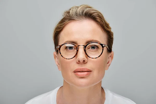 Modelo feminino loira bonita com cabelo loiro e óculos olhando para a câmera no fundo cinza — Fotografia de Stock