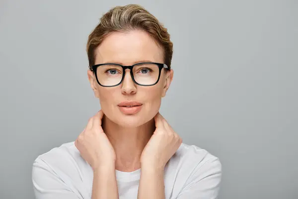 Appealing blonde female model with blonde hair and glasses looking at camera on gray backdrop — Stock Photo