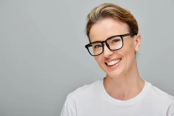 Cheerful attractive woman with blonde hair with glasses smiling happily at camera on gray background — Stock Photo
