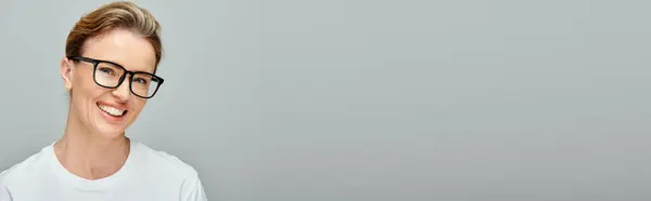 Allegra donna attraente con i capelli biondi con gli occhiali sorridenti alla fotocamera su sfondo grigio, banner — Foto stock