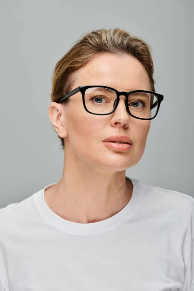 Attraente bionda modello femminile con capelli biondi e occhiali guardando la fotocamera su sfondo grigio — Foto stock