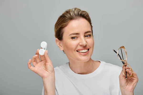 Jolly attractive woman with blonde hair and glasses holding contact lenses and looking away — Stock Photo