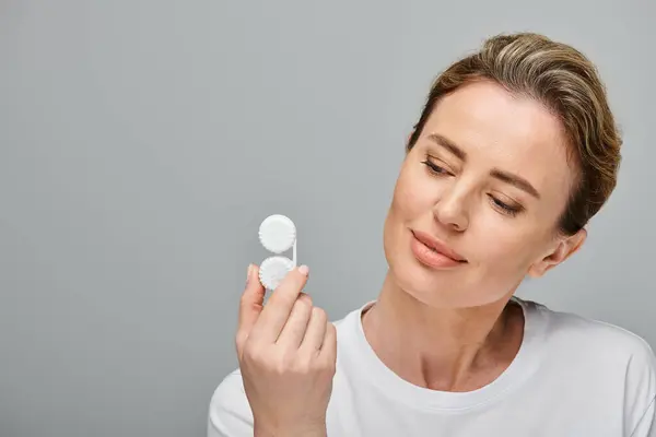 Good looking jolly woman with blonde hair holding contact lenses and looking away on gray backdrop — Stock Photo