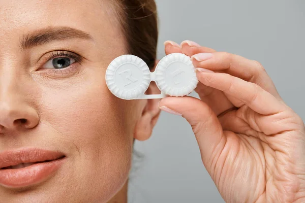 Close up of attractive jolly woman with blonde hair holding contact lenses and looking at camera — Stock Photo