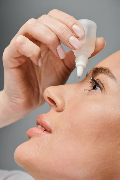 Close up of attractive female model with blonde hair putting in eye drops while on gray backdrop — Stock Photo