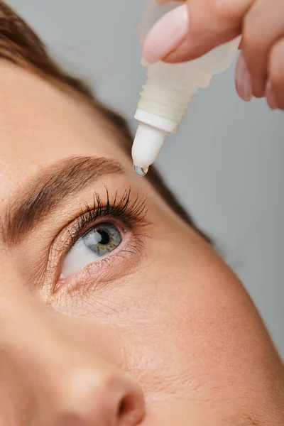 Close up of attractive female model with blonde hair putting in eye drops while on gray backdrop — Stock Photo