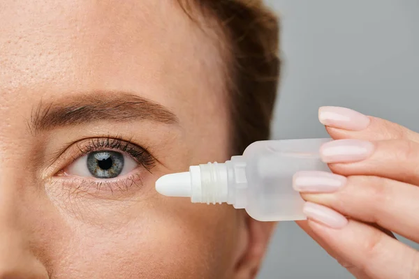 Close up of appealing female model with blonde hair putting in eye drops on gray backdrop — Stock Photo