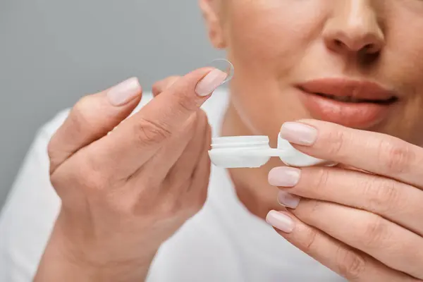 Vue recadrée du modèle féminin concentré portant des lentilles de contact soigneusement sur fond gris — Photo de stock