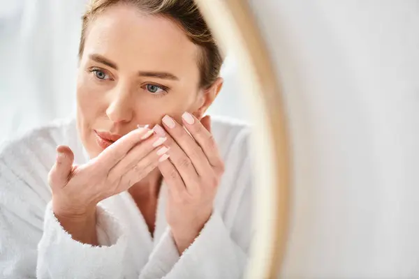 Mulher bonita em roupão de banho confortável branco usando suas lentes de contato perto do espelho no banheiro — Fotografia de Stock
