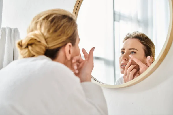 Attractive woman in white comfy bathrobe wearing her contact lenses near mirror in bathroom — Stock Photo