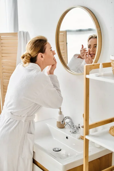 Attraente donna in bianco comodo accappatoio indossa le lenti a contatto vicino specchio in bagno — Foto stock
