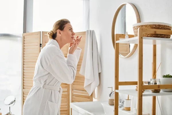 Bella donna in bianco comodo accappatoio indossa le lenti a contatto vicino specchio in bagno — Foto stock
