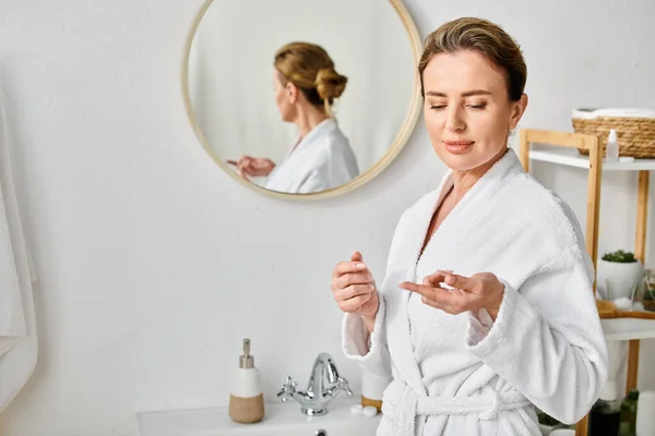 Good looking woman in white comfy bathrobe wearing her contact lenses near mirror in bathroom — Stock Photo