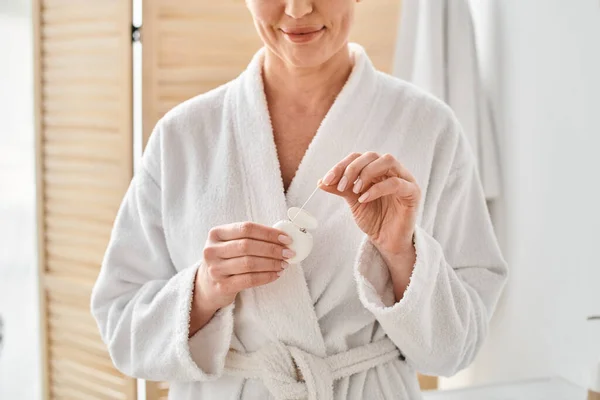 Cropped view of joyful adult woman in bathrobe cleaning her teeth with dental floss in bathroom — Stock Photo