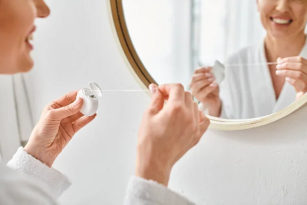 Cropped view of adult woman in cozy bathrobe cleaning her teeth with dental floss in bathroom — Stock Photo