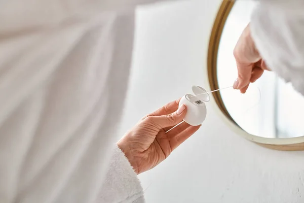 Обрезанный вид взрослой женщины в удобном халате, чистящей зубы зубной нитью в ванной комнате — стоковое фото
