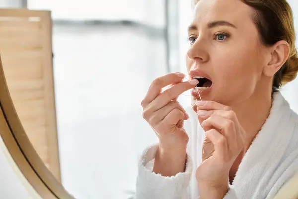 Appealing blonde woman with collected hair in bathrobe cleaning her teeth with dental floss — Stock Photo