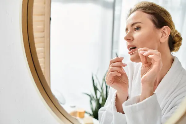 Appealing blonde woman with collected hair in bathrobe cleaning her teeth with dental floss — Stock Photo