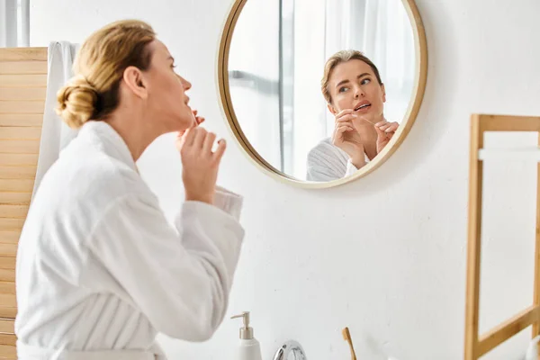 Appealing blonde woman with collected hair in bathrobe cleaning her teeth with dental floss — Stock Photo