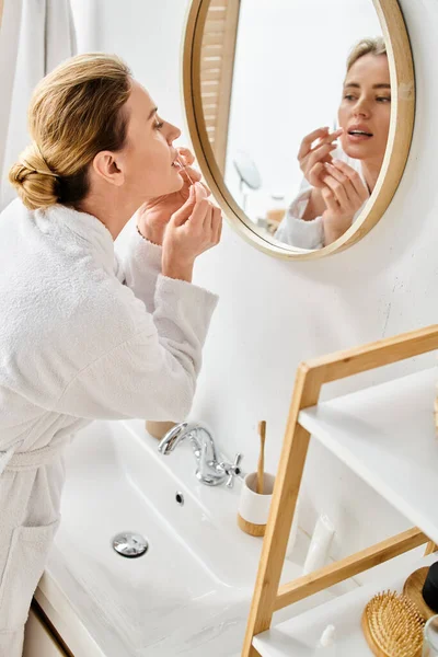 Beautiful blonde woman with collected hair in bathrobe cleaning her teeth with dental floss — Stock Photo