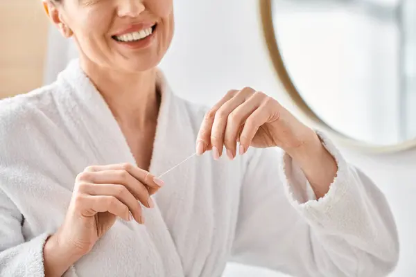 Cropped view of jolly adult woman in bathrobe cleaning her teeth with dental floss in bathroom — Stock Photo