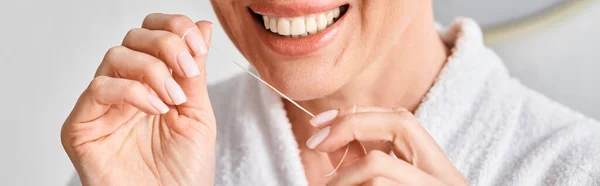 Cropped view of jolly woman in bathrobe cleaning her teeth with dental floss in bathroom, banner — Stock Photo